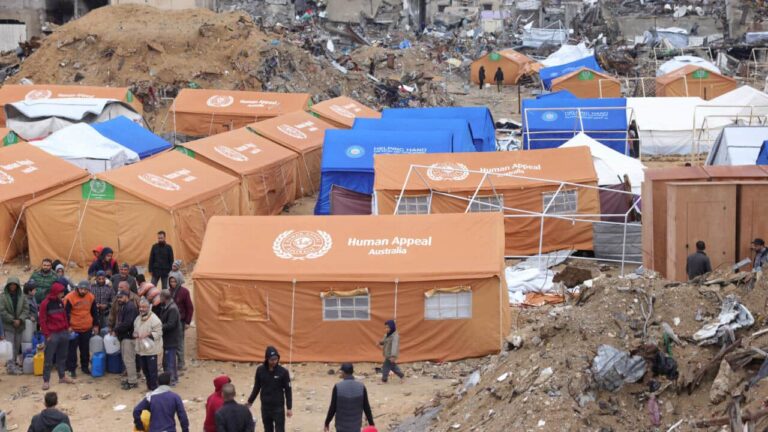 فلسطينيون يحتمون في خيام أقيمت وسط مبانٍ تضررت بشدة يحملون عبوات بلاستيكية لملئها بالمياه في جباليا في شمال قطاع غزة في 6 فبراير 2025.
