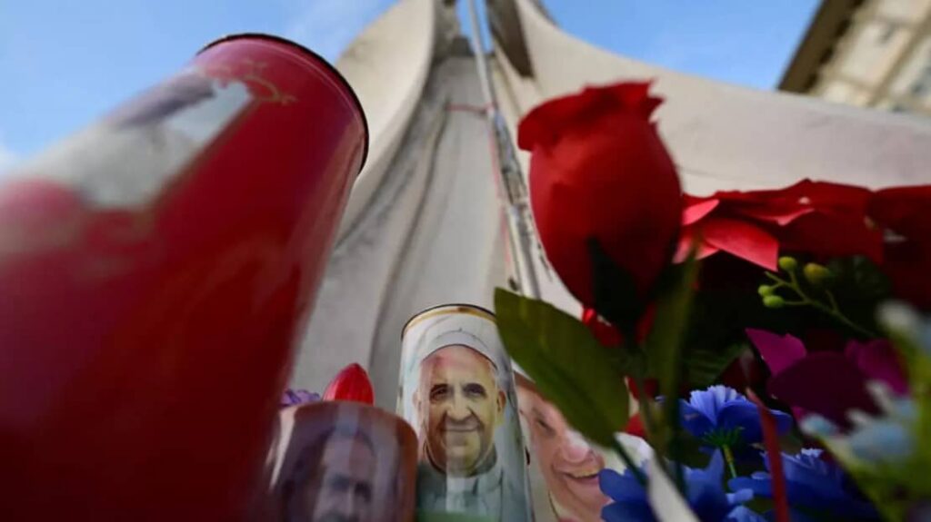 شموع وزهور وصور للبابا فرانسيس عند تمثال البابا يوحنا بولس الثاني خارج مستشفى جيميلي في روما حيث يعالج البابا فرانسيس. 28 فبراير 2025.